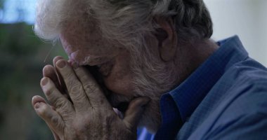 Yaşlı bir adam dua ya da keder anında, eller birarada ve gözler kapalı, keder ve iç mekan içinde iç gözlem ifade