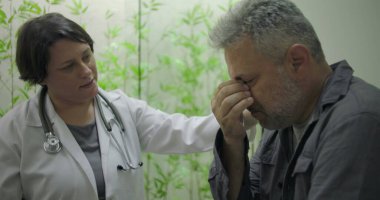 Klinikte tıbbi danışmanlık sırasında zor durumda olan orta yaşlı erkek hastaya destek veren kadın doktor