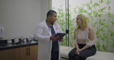 Parlak klinikte dijital tablet kullanan orta yaşlı kadın hastaya danışmanlık yapan erkek doktor, açık iletişimi teşvik ediyor ve kişiselleştirilmiş tıbbi bakım