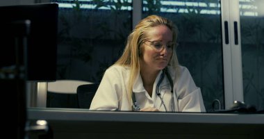 Gece vardiyası sırasında zor durumdaki kadın doktor, yoğun duygusal baskıyla karşı karşıya klinik ortamda otururken, ezici iş yükü ile boğuşurken,