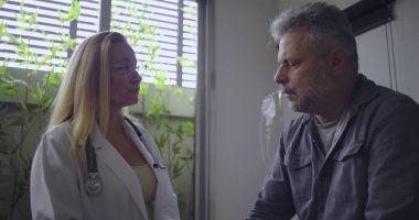 Klinikteki tıbbi muayene sırasında orta yaşlı erkek hastaya zor teşhisler koyan kadın doktor.