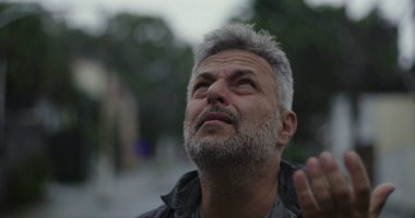 Yukarı bakan orta yaşlı bir adam, yağmurda ellerini kaldırmış, duygusal sorgulama ya da ruhani bir katman.