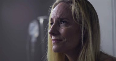 Klinik ortamda gözyaşlarını tutan kadının yakın plan çekimi, keder ve acıyla dolu ifade, yüzünde ve postomda hafif gerilim