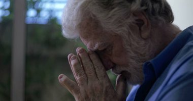 Başı öne eğik yaşlı bir adam özel dua anında ellerini birbirine bastırıyor ya da pencerenin yakınındaki sessiz mekanda kederli bir yansıma