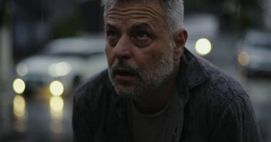 Yukarı bakan orta yaşlı bir adam, yağmurda ellerini kaldırmış, duygusal sorgulama ya da ruhani bir katman.