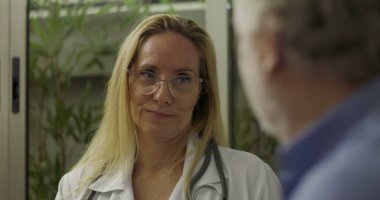 Kadın doktor, modern clini 'deki sağlık hizmetleri tartışması sırasında üst düzey erkek hastayla konuşurken düşünceli bir ifade takınıyor.