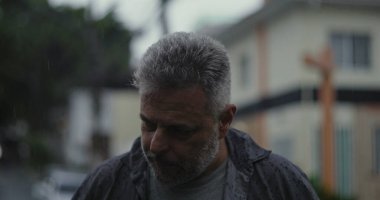 Orta yaşlı bir adam endişeli bir ifadeyle, gergin duruşu ve şehir sokaklarında duygusal ağırlığıyla yan yana bakıyor.