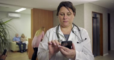 Hasta ve resepsiyonistle birlikte hastane lobisinde gülümserken akıllı telefon kullanan kadın doktor