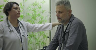 Klinikte tıbbi danışmanlık sırasında zor durumda olan orta yaşlı erkek hastaya destek veren kadın doktor