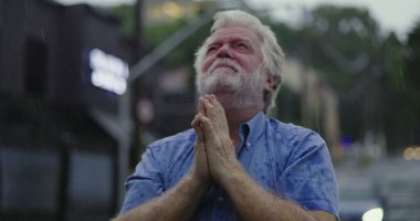 Yağmurun altında başıyla acı çeken yaşlı bir adam, gözleri kapalı, duygusal acı ve umutsuzlukla boğulmuş bir ifade.