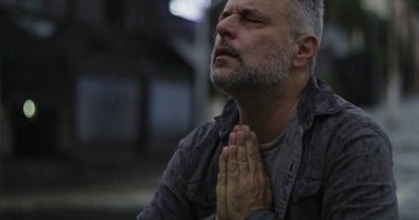 Orta yaşlı, gözleri kapalı ve elleri umutsuzca dua eden ya da duygusal yalvaran, rai 'de duran bir adam.