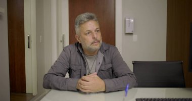 Doktor, tıp bürosunda kağıt ve cam masadaki belgelerle baş başa görüşmede orta yaşlı bir hastaya hitap ediyor.