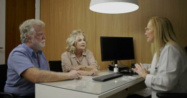 Özel sağlık bürosundaki detaylı sağlık randevusu sırasında yaşlı çiftle ilaç planını tartışan kadın doktor.