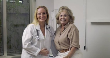 Doktor ve yaşlı hasta gülümsüyor ve tıbbi muayene sırasında sıcak bir anı paylaşıyor. Hastanenin muayene odasında.