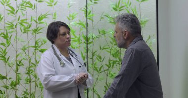 Kadın doktor, sağlık danışmanlığı sırasında orta yaşlı erkek hastayla iletişim kuruyor, profesyonel tıp ortamında rehberlik ve netlik sağlıyor.