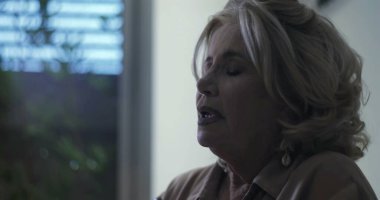 Suni teneffüs yapan yaşlı bir kadın. Gözleri açık ve kaşları hafif kalkık. Kapalı mekanlarda endişeli ve gergin duygular sergiliyor.