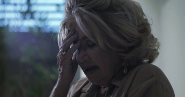 Duygusal yorgunluk ifadesiyle alnına dokunan yaşlı bir kadın ya da kapalı bir ortamda ezici bir stres.