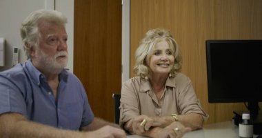 Özel sağlık bürosundaki detaylı sağlık randevusu sırasında yaşlı bir çiftle ilaç planını tartışan kadın doktor