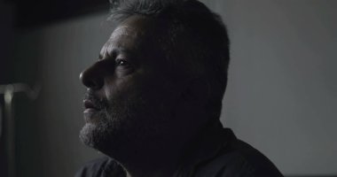 Karanlık klinikte eli yüzü kapalı sıkıntılı bir adamın yakın çekimi, tanıya karşı duygusal tepki ya da düşük ışıkta yakalanan iç kargaşa