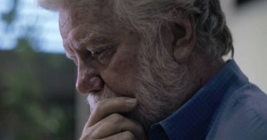 Yaşlı bir adam derin bir yansımayla çenesini dinlendirirken, gözleri sessiz düşünceli bir anda aşağıya odaklanmış.