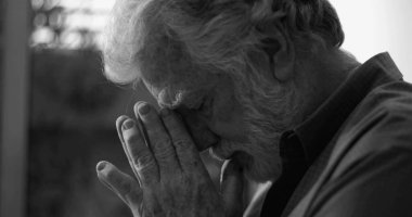 Siyah beyaz giyinmiş yaşlı bir adam gözleri kapalı ve elleri kutsal dualarla sımsıkı sarılmış ya da pencerenin yanında derin duygusal yansımalar içinde.