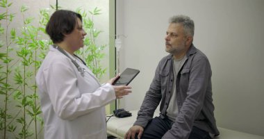 Klinik konsültasyonu sırasında erkek hastaya tıbbi bilgileri açıklamak için tablet kullanan doktor, açık iletişim ve hasta bağlarını vurguladı