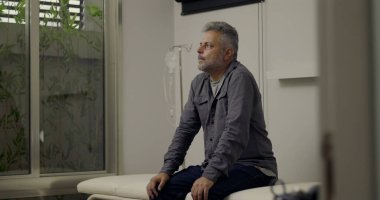 Muayenehanede muayene masasında tek başına oturan bir adam, danışmadan sonra duyguları incelerken sessizce yukarıya doğru bakan, sırtüstü serumla görülebilen bir serum.