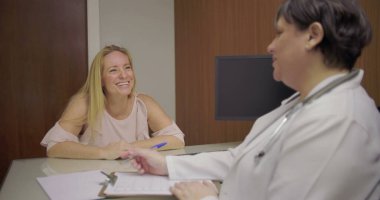 Klinikteki danışma masasında doktorla konuşurken gülümseyen orta yaşlı bir hasta.