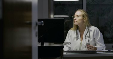Kadın doktor gece geç saatlere kadar tıp ofisinde çalışıyor, klavyeye yazıyor, odaklanmış ve konsantre olmuş, profesyonel sağlık hizmetleri ortamı