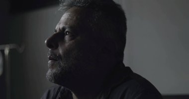 Karanlık klinikte eli yüzü kapalı sıkıntılı bir adamın yakın çekimi, teşhislere karşı duygusal tepki ya da düşük ışıkta yakalanan iç kargaşa