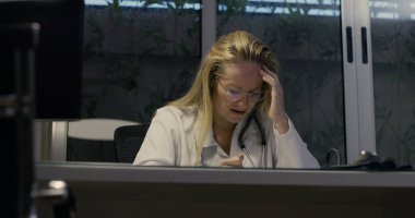 Kadın doktor umutsuzca başını eğiyor. Gece klinikte şiddetli yorgunluk belirtileri gösteriyor.