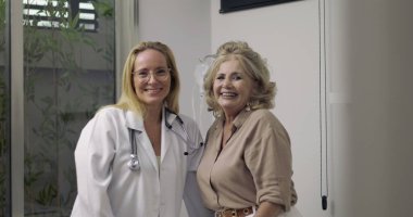 Doktor ve yaşlı hasta gülümsüyor ve tıbbi muayene sırasında sıcak bir anı paylaşıyor. Hastanenin muayene odasında.