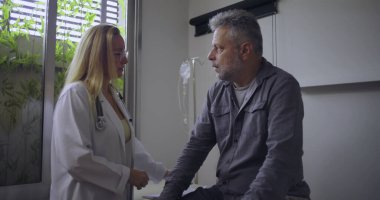 Klinikteki tıbbi muayene sırasında orta yaşlı erkek hastaya zor teşhisler koyan kadın doktor.