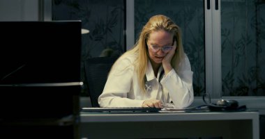 Kadın doktor gece geç saatlere kadar çalışırken masaya yaslanıyor. Yorgun ve bitkin görünüyor.