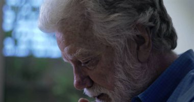 Umudun ve yansımanın yumuşak ifadesiyle yukarı bakan yaşlı bir adam, yan profili çerçevelenmiş, kapalı arka planda nazik