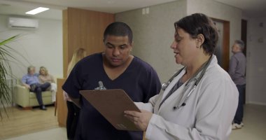 Doktor ve hemşire hastane koridorunda hasta çizelgesini birlikte gözden geçiriyorlar. Her gün yoğun odaklanma ve tıbbi ekip çalışması ile birlikte.