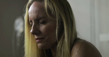 Kadın, sağlık hizmetleri çevresindeki bir anlık yansıma sırasında, gözleri kapalı, tek başına zor duyguları sindirerek sessizce tıbbi odada oturuyor.