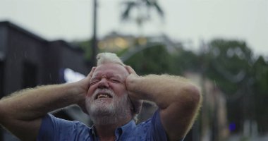Yağmurun altında başıyla acı çeken yaşlı bir adam, gözleri kapalı, duygusal acı ve umutsuzlukla boğulmuş bir ifade.