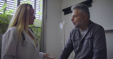 Klinikteki tıbbi muayene sırasında orta yaşlı erkek hastaya zor teşhisler koyan kadın doktor.