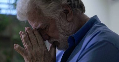 Başı öne eğik yaşlı bir adam özel dua anında ellerini birbirine bastırıyor ya da pencerenin yakınındaki sessiz mekanda kederli bir yansıma