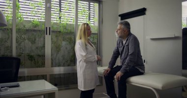 Doktor klinik atama sırasında oturmakta olan erkek hastaya konan teşhisi sakince tartışıyor. Parlak modern muayene odasında destekleyici bir konuşma yapılıyor.