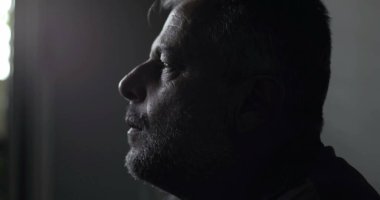 Düşük ışık kliniğindeki orta yaşlı adamın yakın çekimi, düşünceli sükûnetten duygusal sıkıntıya geçiş, teşhis ve içsel turmoilere karşı sessiz tepkiler.