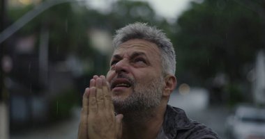 Yukarı bakan orta yaşlı bir adam, yağmurda ellerini kaldırmış, duygusal sorgulama ya da ruhani bir katman.