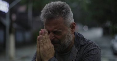 Orta yaşlı, gözleri kapalı ve elleri umutsuzca dua eden ya da duygusal yalvaran, rai 'de duran bir adam.