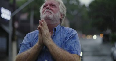 Yağmurun altında başıyla acı çeken yaşlı bir adam, gözleri kapalı, duygusal acı ve umutsuzlukla boğulmuş bir ifade.