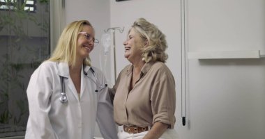 Doktor ve yaşlı hasta gülümsüyor ve tıbbi muayene sırasında sıcak bir anı paylaşıyor. Hastanenin muayene odasında.