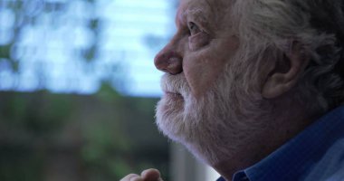 Umudun ve yansımanın yumuşak ifadesiyle yukarı bakan yaşlı bir adam, yan profili çerçevelenmiş, kapalı arka planda nazik