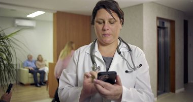 Hasta ve resepsiyonistle birlikte hastane lobisinde gülümserken akıllı telefon kullanan kadın doktor