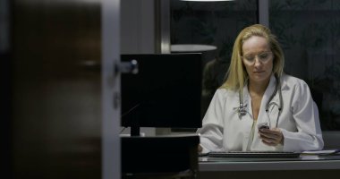Kadın doktor gece geç saatlere kadar tıp ofisinde çalışıyor, klavyeye yazıyor, odaklanmış ve konsantre olmuş, profesyonel sağlık hizmetleri ortamı