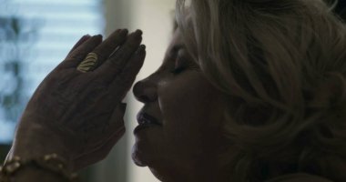 Elleri yüzü kapamış yaşlı bir kadın, gözleri sessiz duygusal keder ya da dua anlarında kapalı.